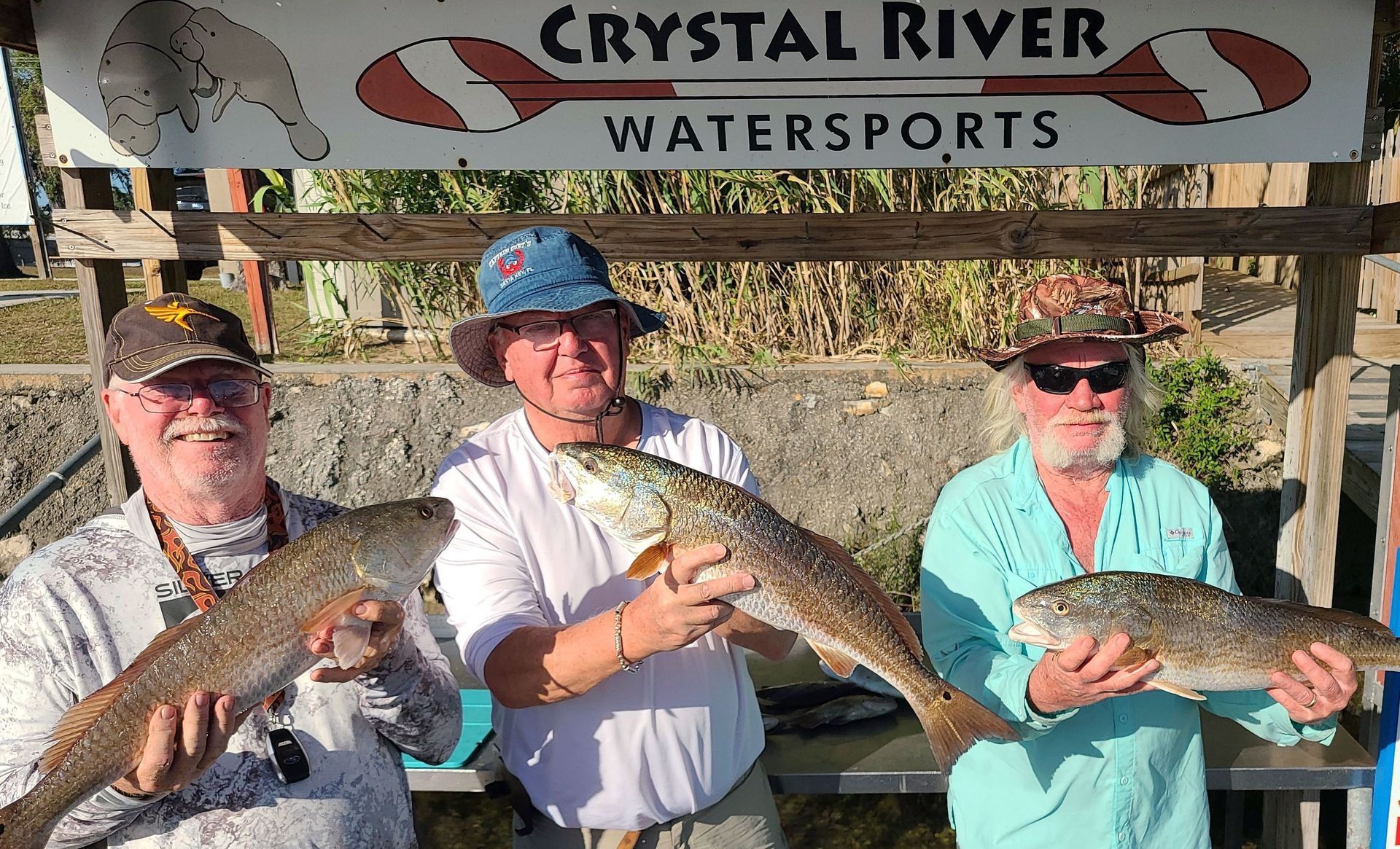 Three men are holding fish in front of a crystal river watersports sign.