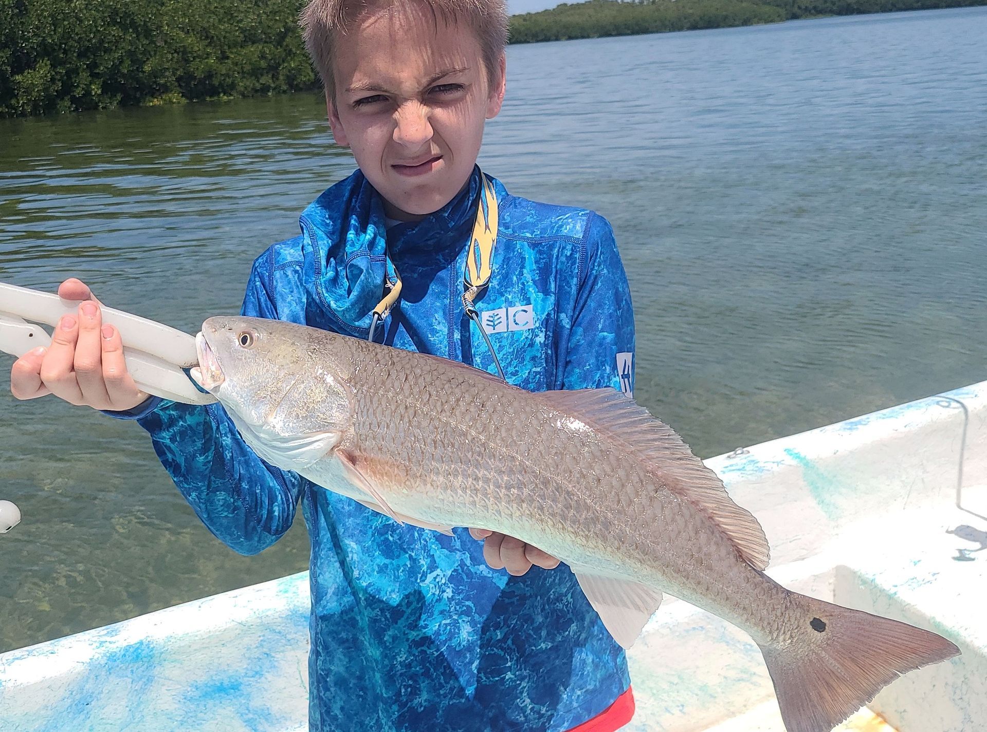 A young boy is holding a large fish on a boat.
