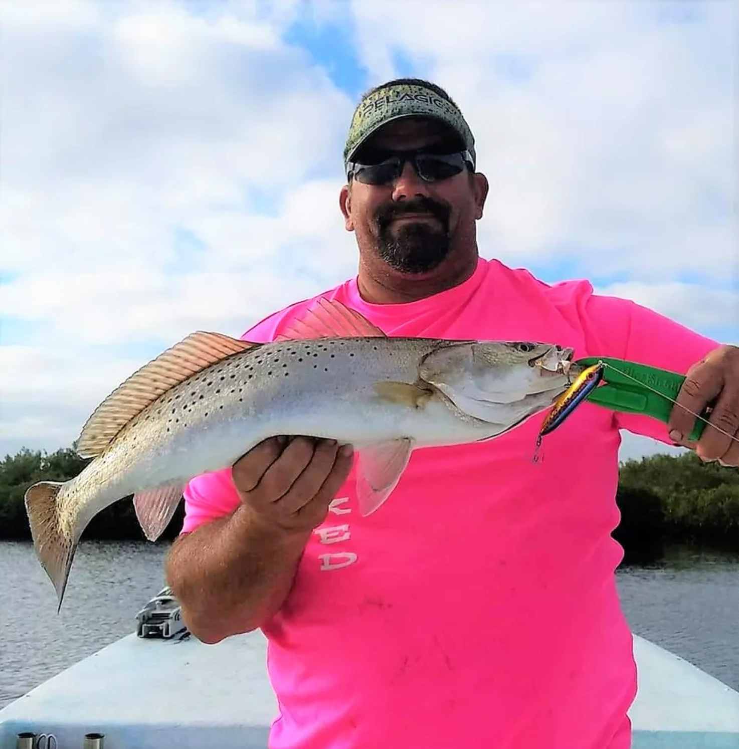 A man in a pink shirt is holding a fish on a boat.