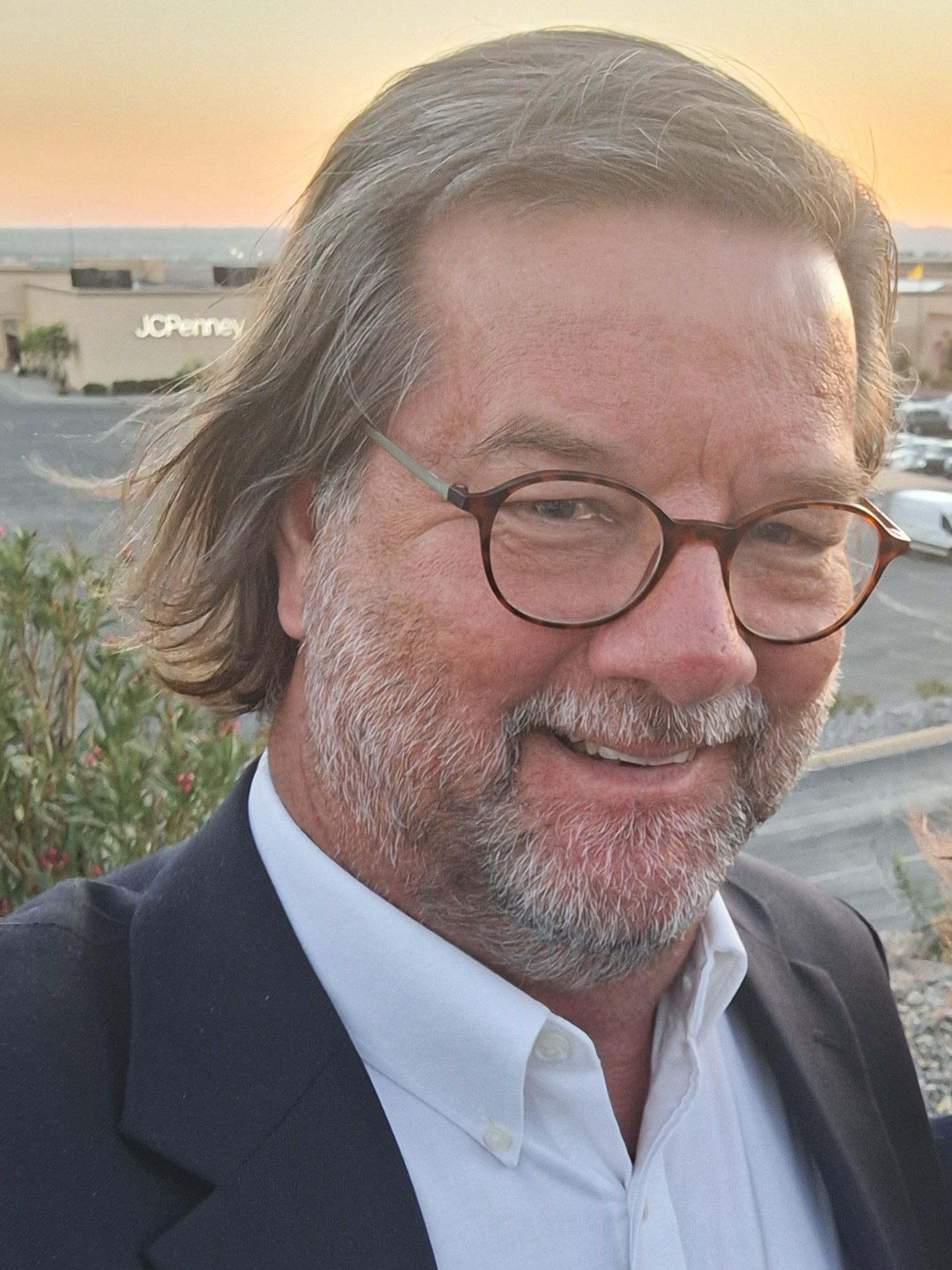 A man wearing glasses and a suit is smiling for the camera.