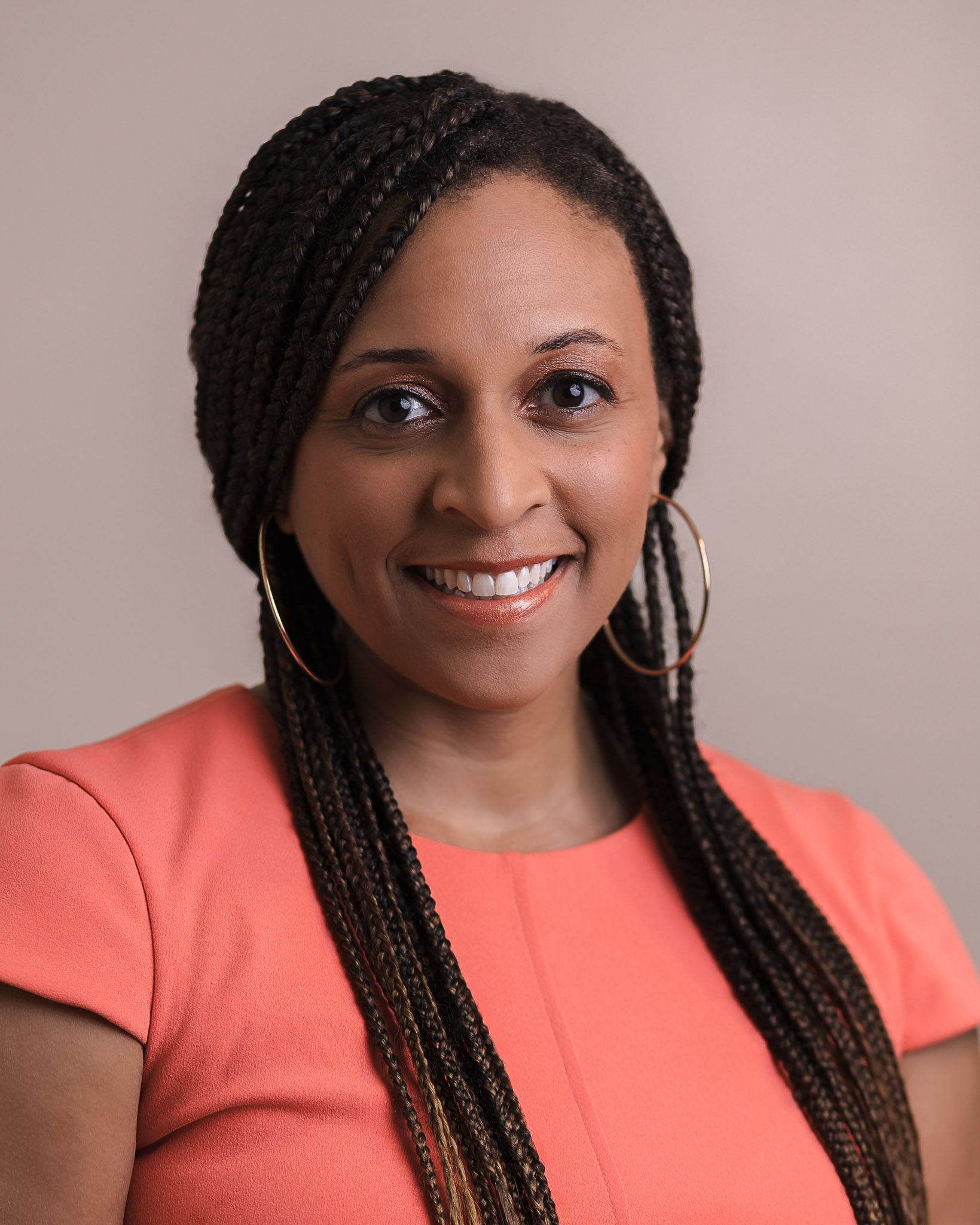 A woman with braids and hoop earrings is smiling for the camera.