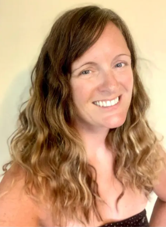 A woman with long curly hair is smiling for the camera.