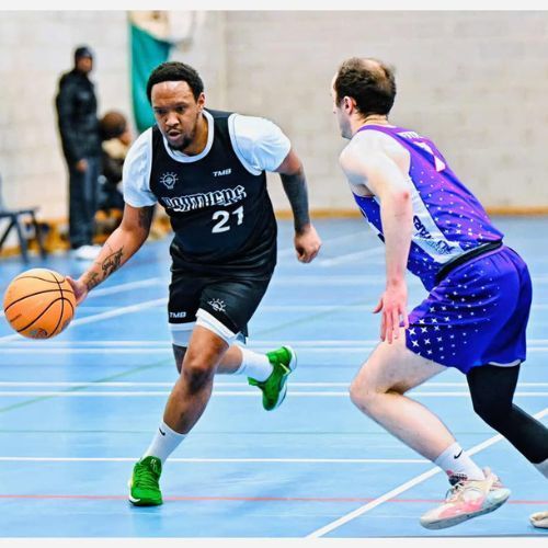 Basketball player dribbling a ball on a court; green shoes, gray shirt, black shorts.