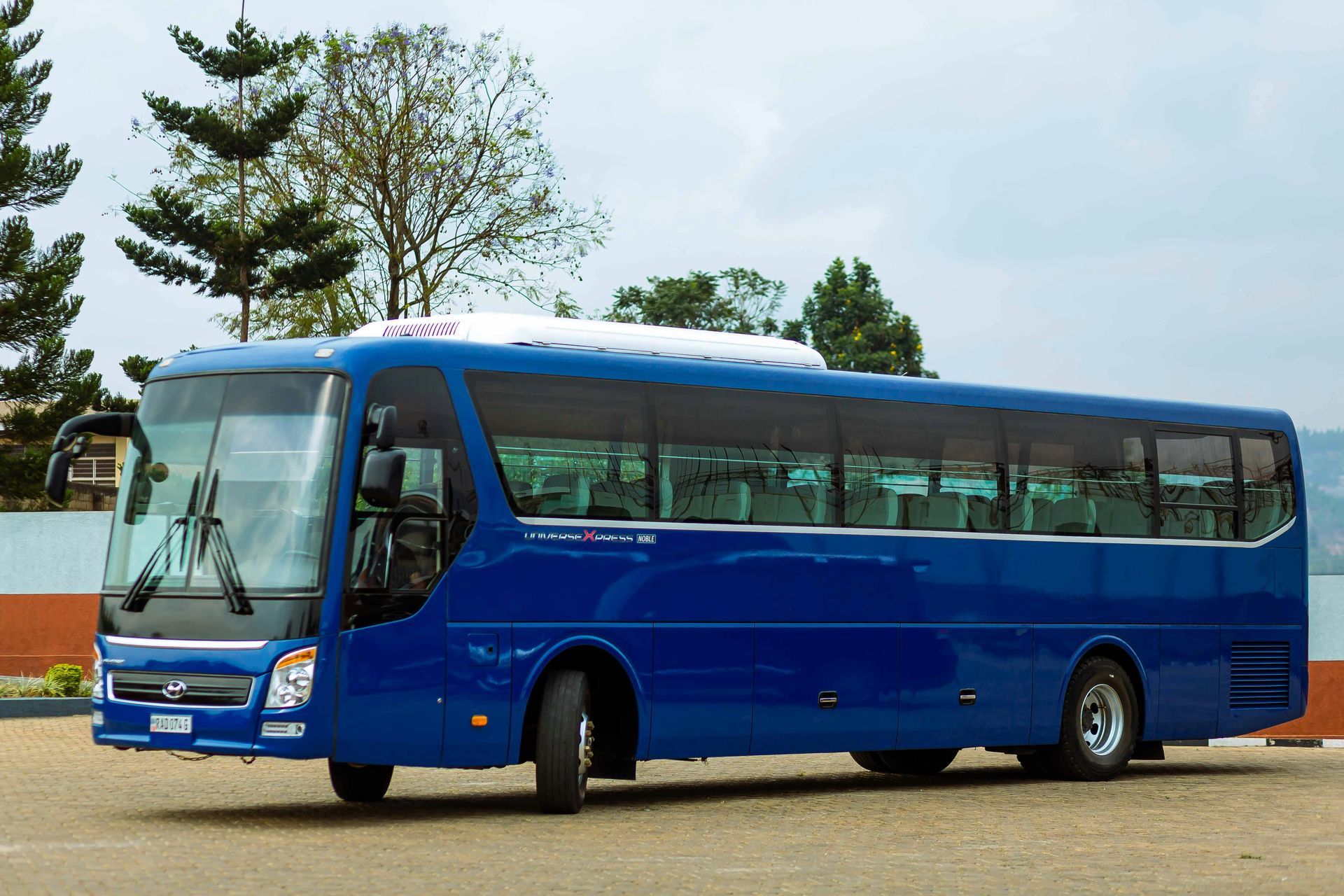A shiny blue charter bus parked on a gravel lot under a bright, partly cloudy sky.