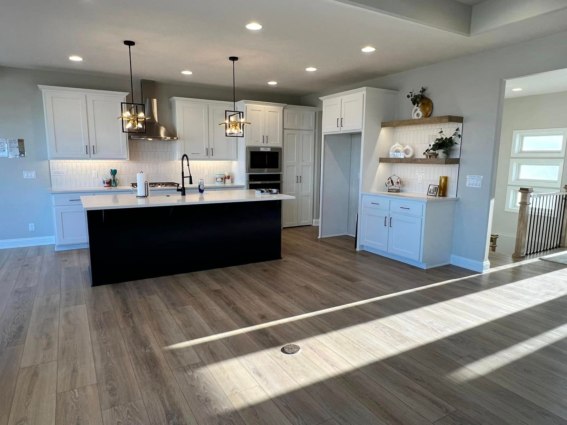 Bright modern kitchen with white cabinets, dark island, pendant lights, and sunlit wood floors