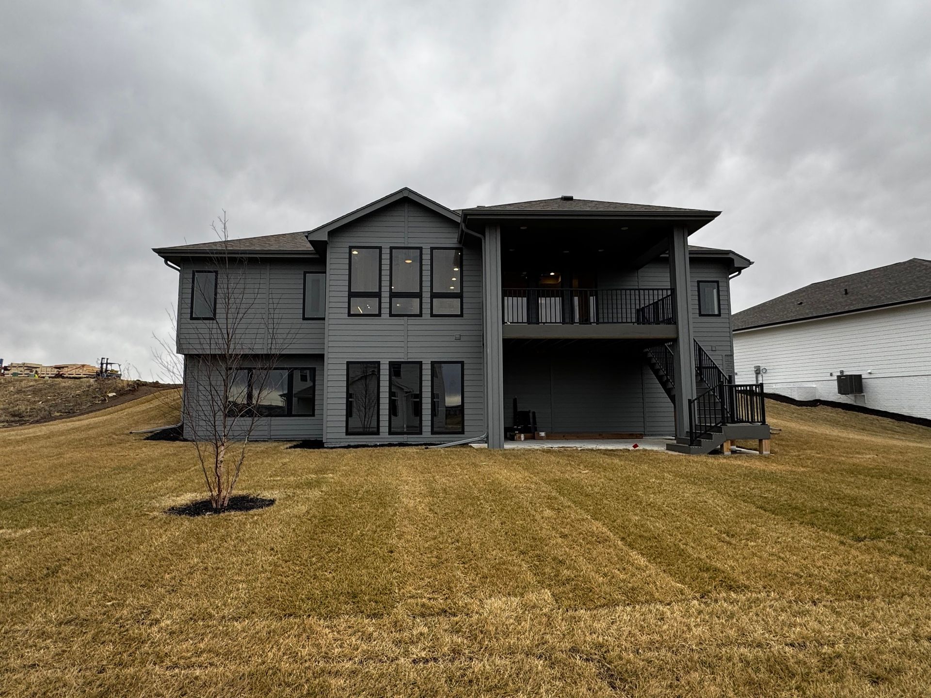 Gray two-story house with a covered balcony on a cloudy day, overlooking a sloped lawn