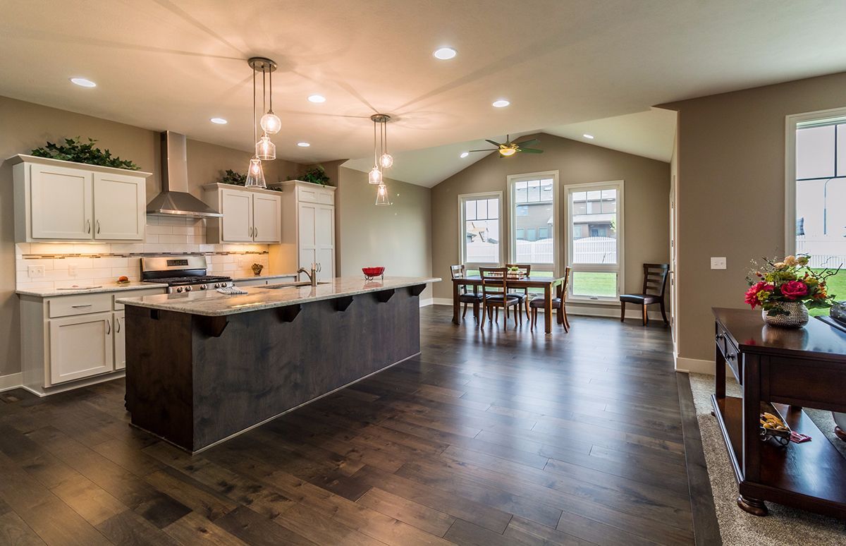 Spacious open-concept kitchen and dining area with dark wood floors, island, and bright windows
