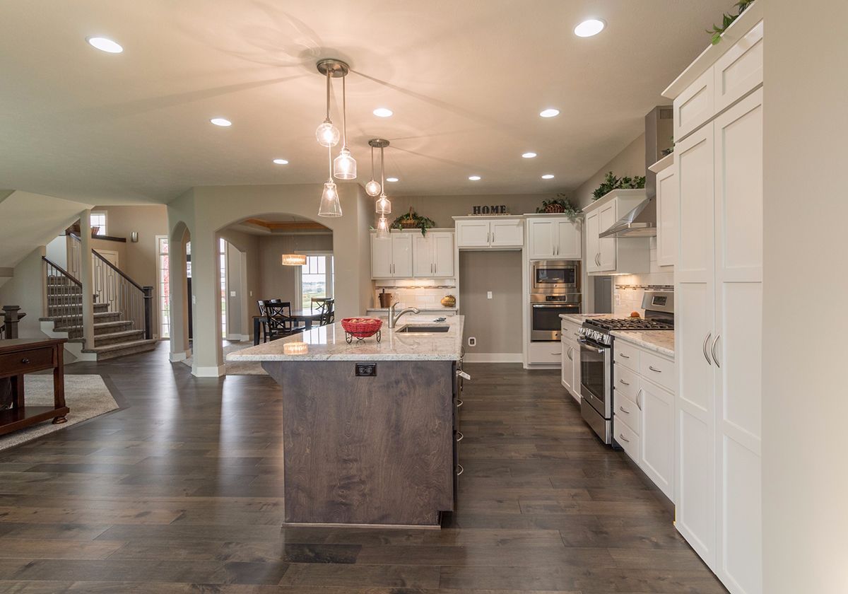 Modern open-concept kitchen with white cabinets, dark wood floors, and a large island under pendant lights