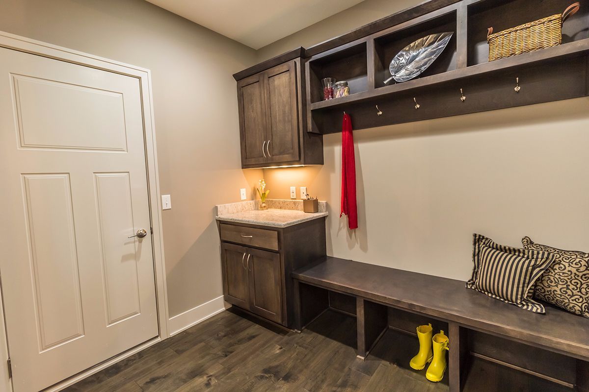 Mudroom with built-in bench, cabinets, sink, and coat hooks, featuring boots and a red towel