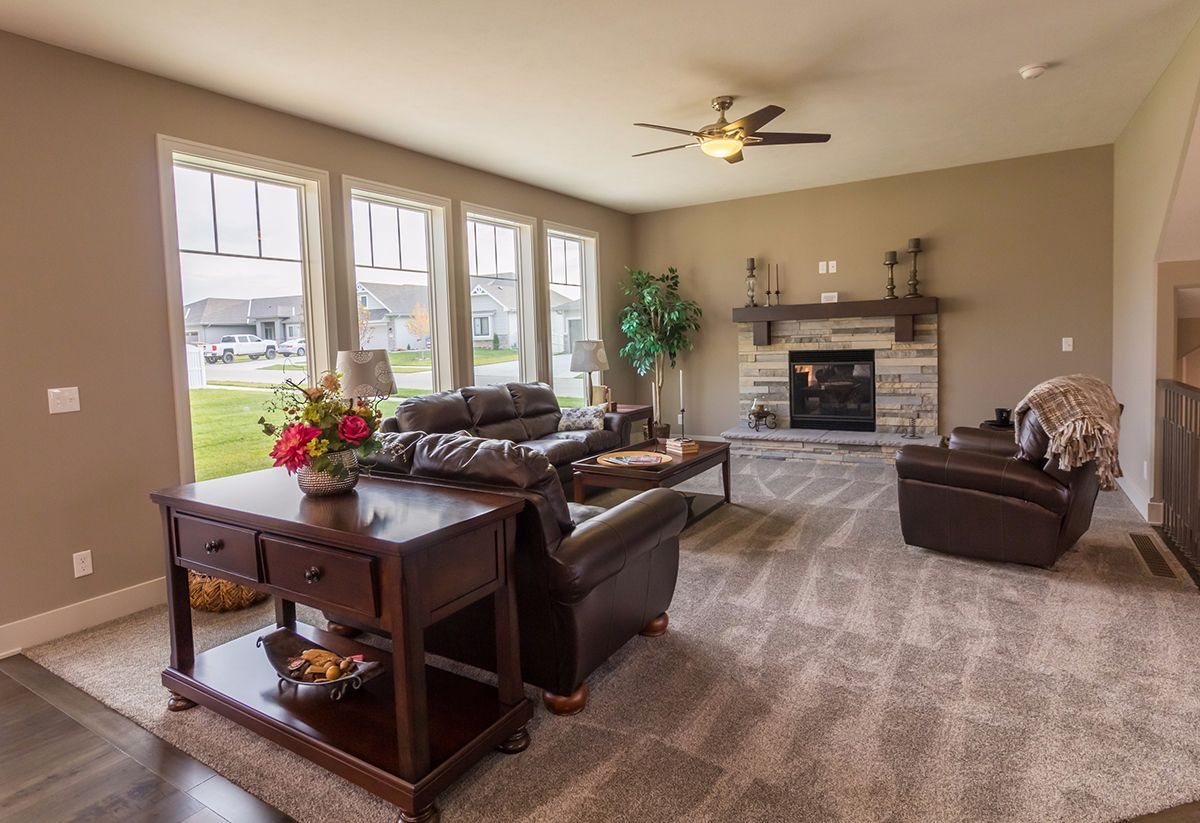 Spacious living room with beige carpet, brown sofas, large windows, and a stone fireplace.