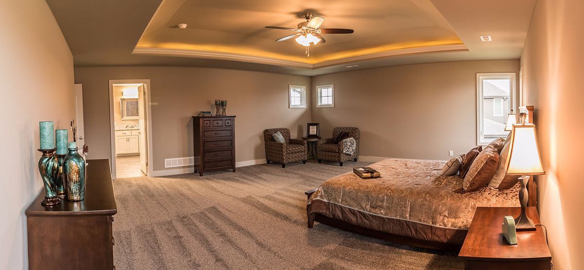 Spacious beige bedroom with a large bed, dresser, ceiling fan, and bedside lamp
