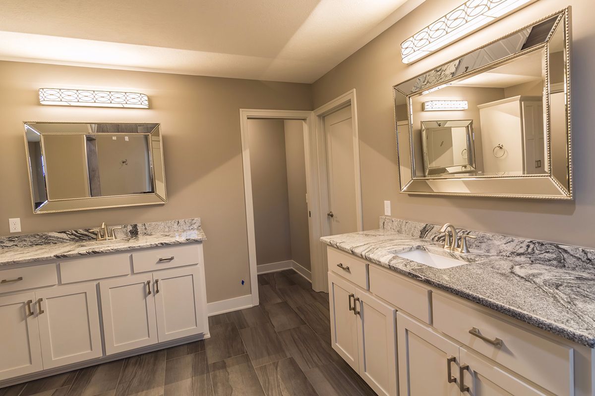 Bright double-vanity bathroom with beige walls, white cabinets, granite countertops, and large mirrors