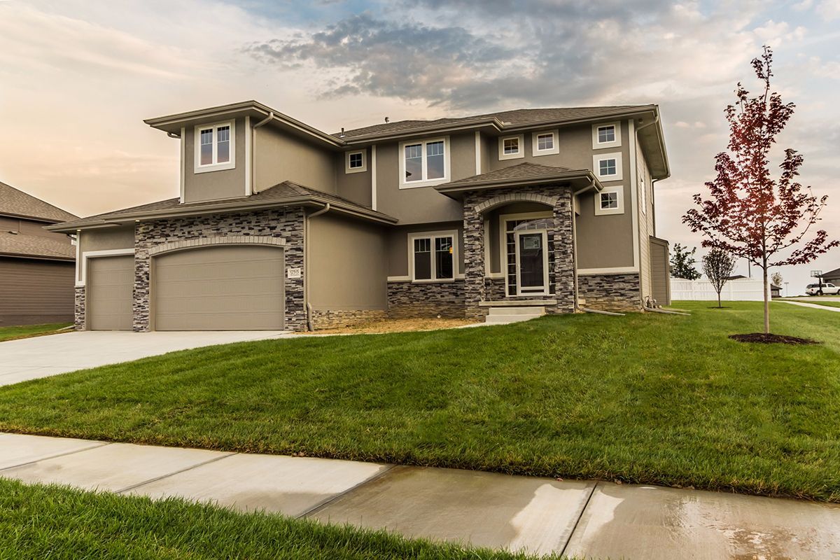 Modern two-story beige house with stone accents and a three-car garage on a green lawn at dusk