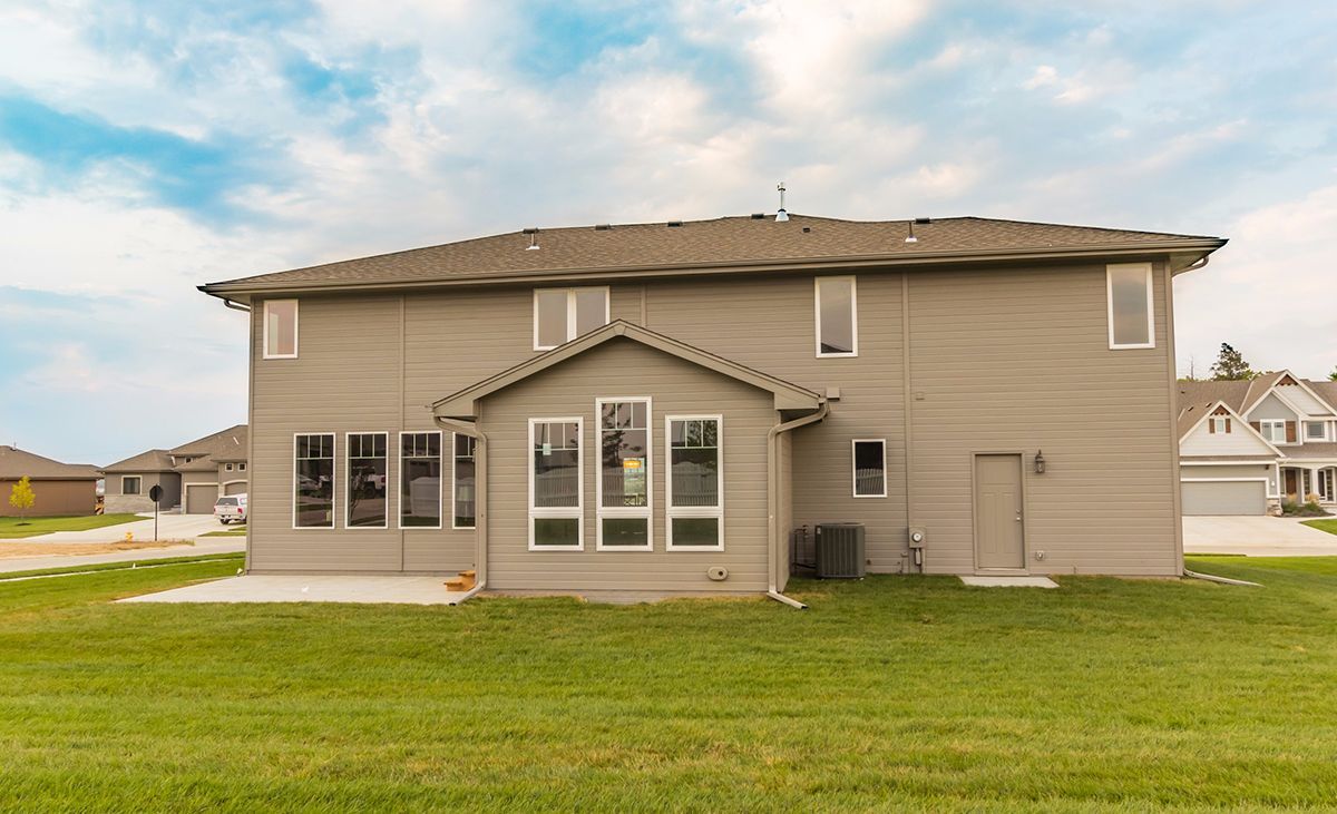 Back view of a beige two-story house with a small patio and green lawn under a cloudy sky