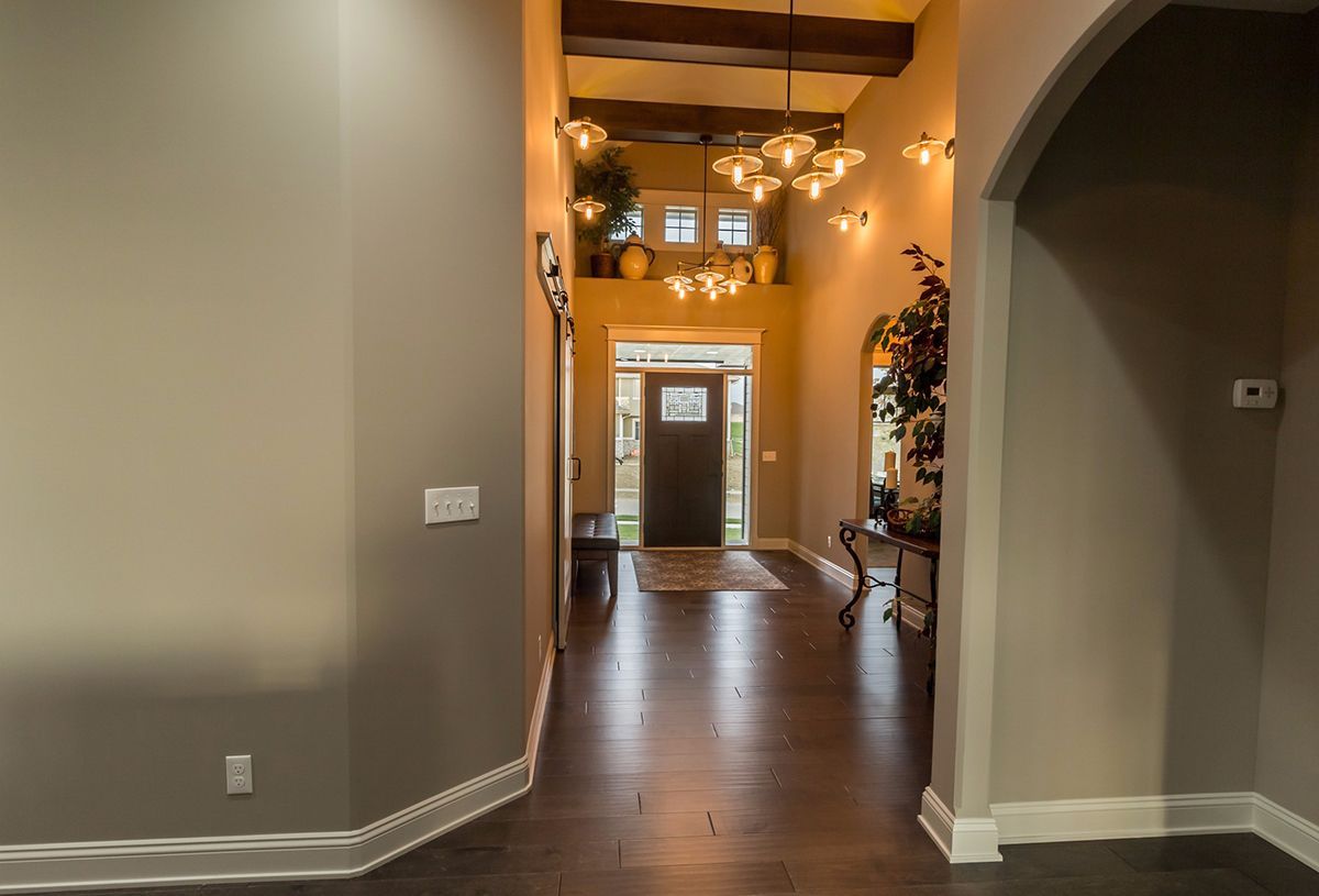 Spacious foyer with hardwood floors, arched doorway, and a view to a front door with warm hanging lights.