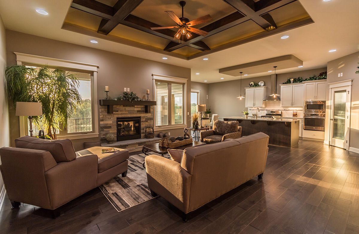 Open-concept living room and kitchen with dark wood floors, brown sofas, fireplace, and ceiling fan lights