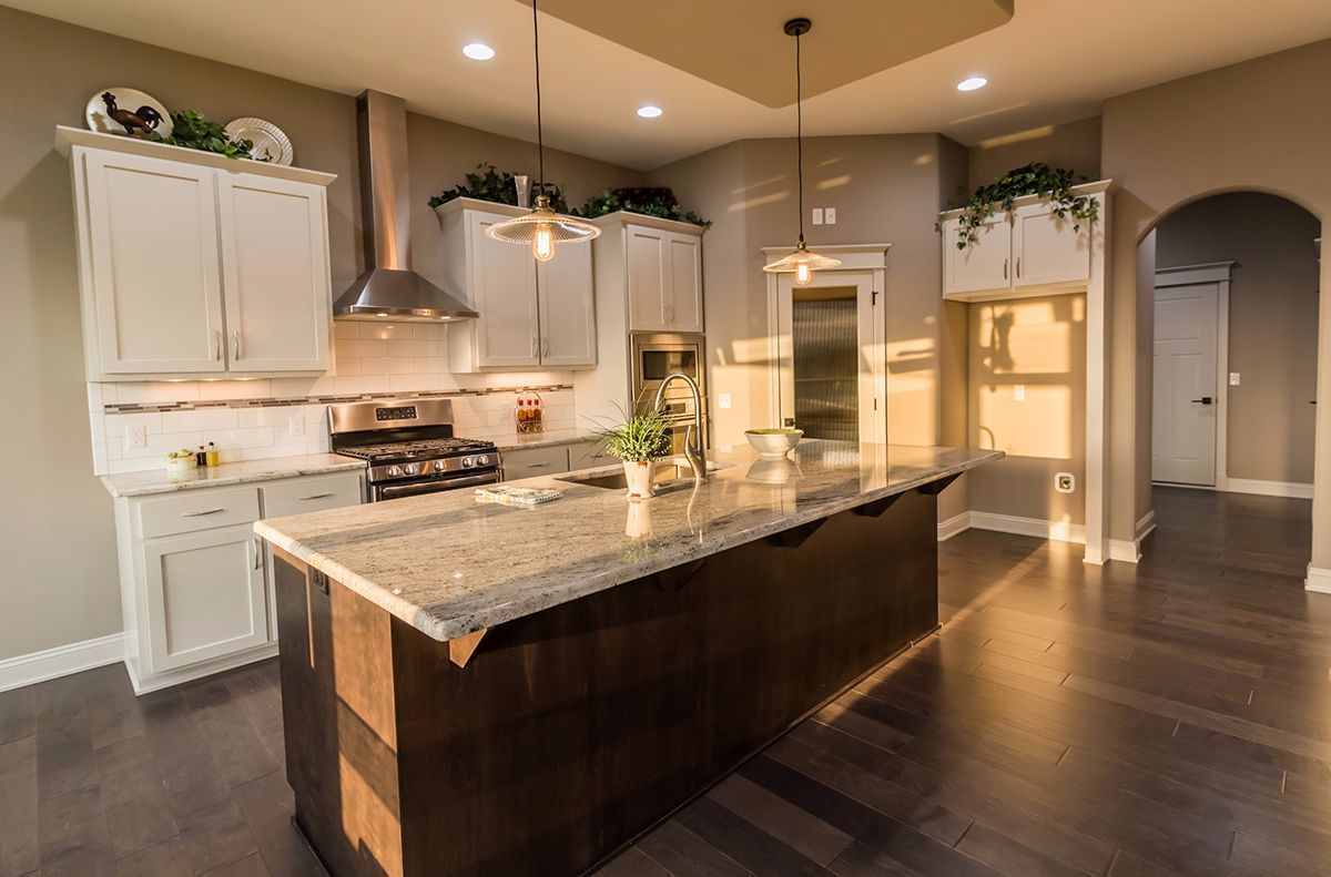 Modern kitchen with granite island, white cabinets, stainless range hood, and dark hardwood floors.