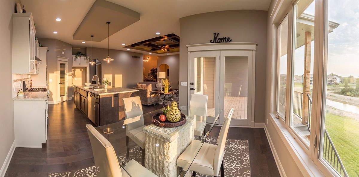 Bright modern kitchen and dining area with granite island, chandelier, and large windows overlooking a road