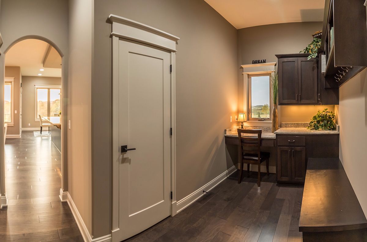 Modern apartment hallway with a white door, dark wood floors, and a small dining nook with warm lighting.