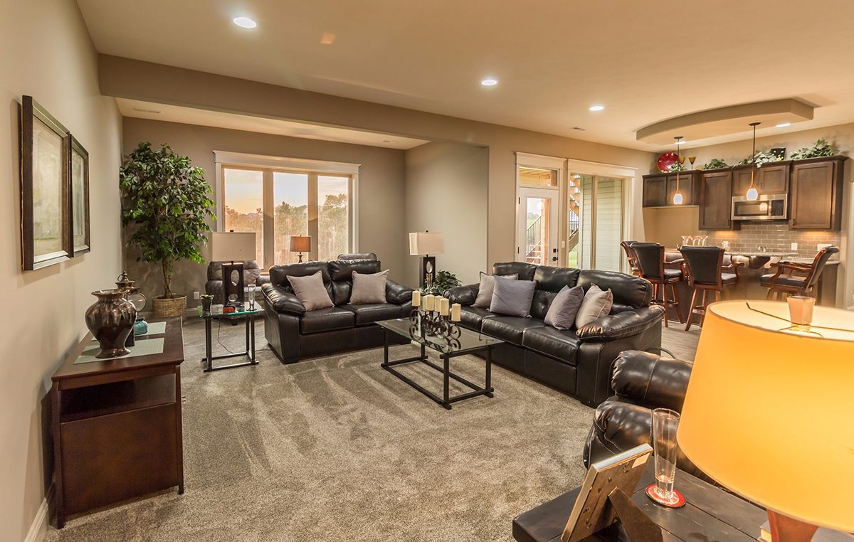 Spacious living room with gray sectional sofa, coffee table, carpet, and open kitchen in warm lighting