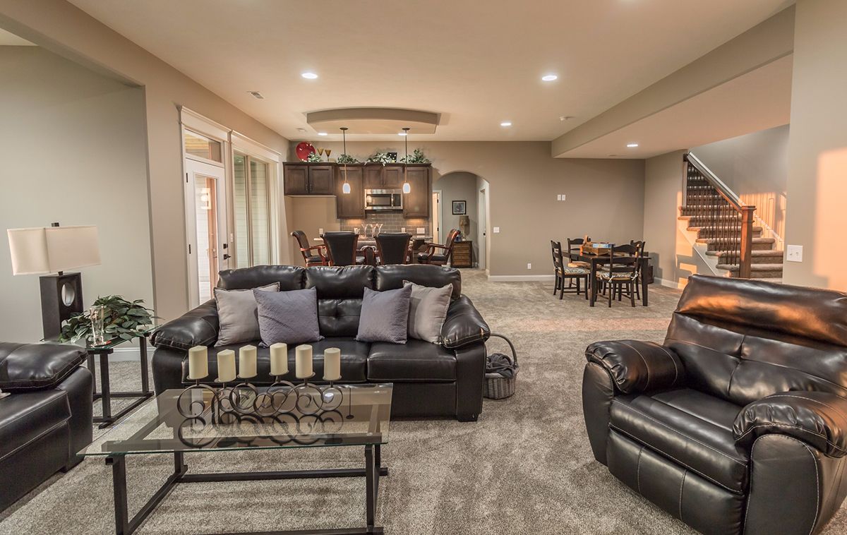 Spacious living room with dark leather sofas, glass coffee table, and open dining area in the background