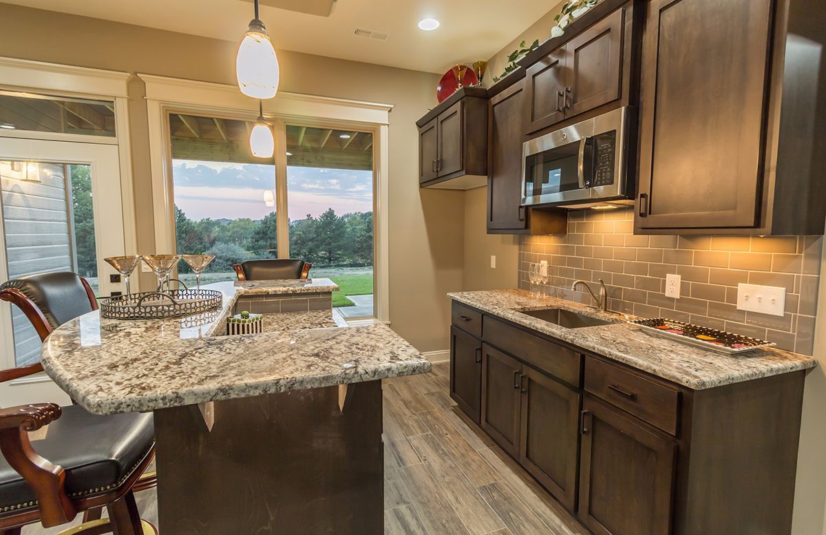 Modern kitchen with dark cabinets, granite island, pendant lights, and large windows overlooking a scenic view