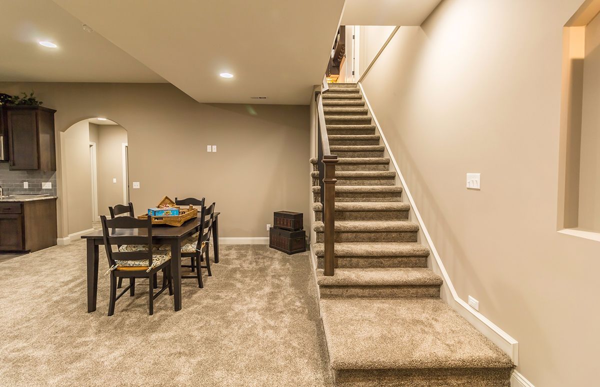 Finished basement with carpeted stairs, dining table, and kitchenette under recessed lighting.
