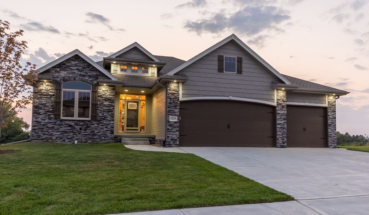 Modern suburban house with stone accents, lit front entry, and a two-car garage at dusk