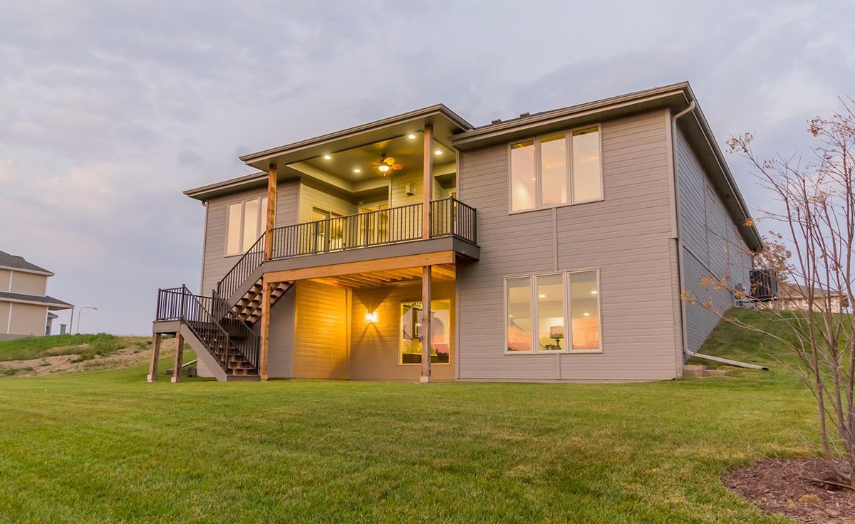 Modern two-story house with lit porch and balcony at dusk, viewed from a grassy yard
