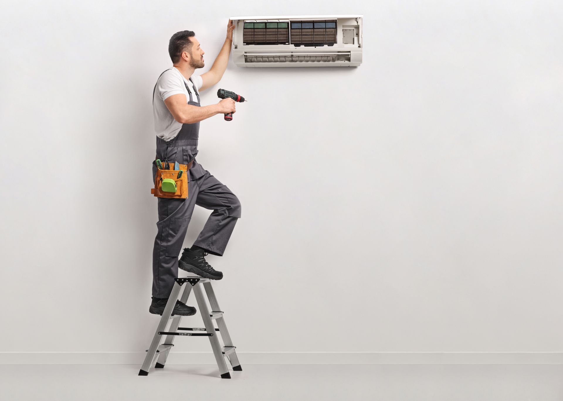 Flame Sensor Repair — Man Repairing Air Conditioner in West Palm Beach, FL A technician standing on a stepladder using a drill to service a wall-mounted AC unit indoors