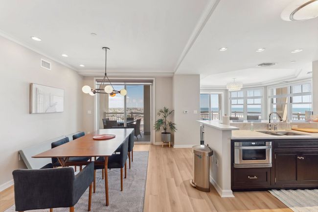 Dining area and kitchen with a table, chairs, and appliances. A balcony with a view is visible.