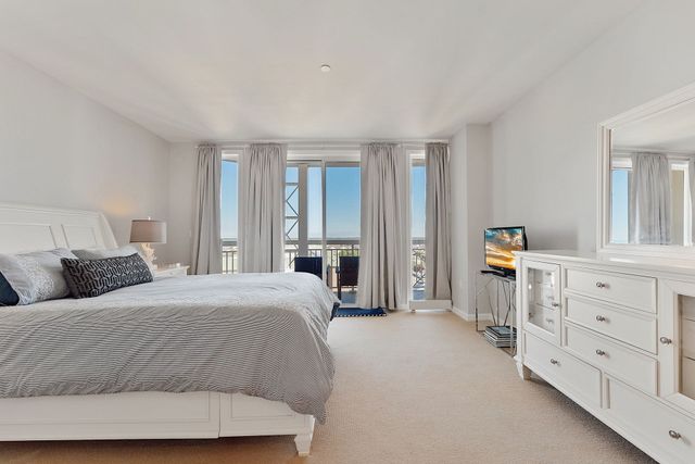 Spacious bedroom with white walls, bed, dresser, and balcony access with city view.