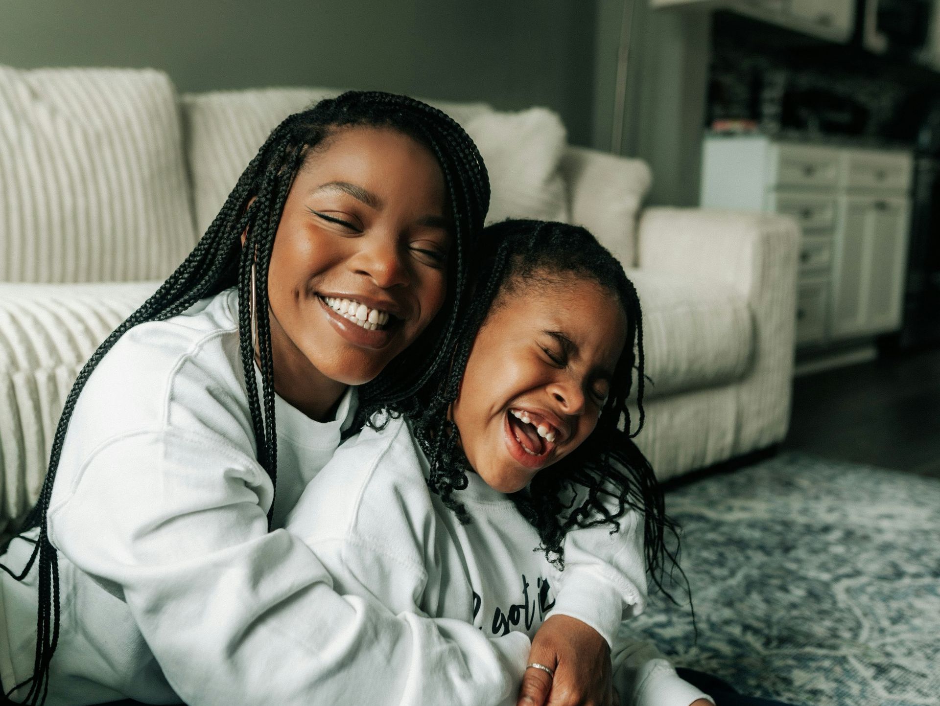 A mother and daughter are laughing together while sitting on the floor.