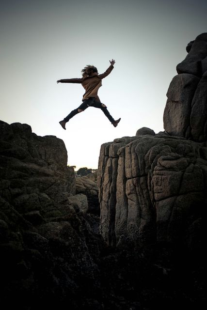 A person is jumping over a rocky cliff