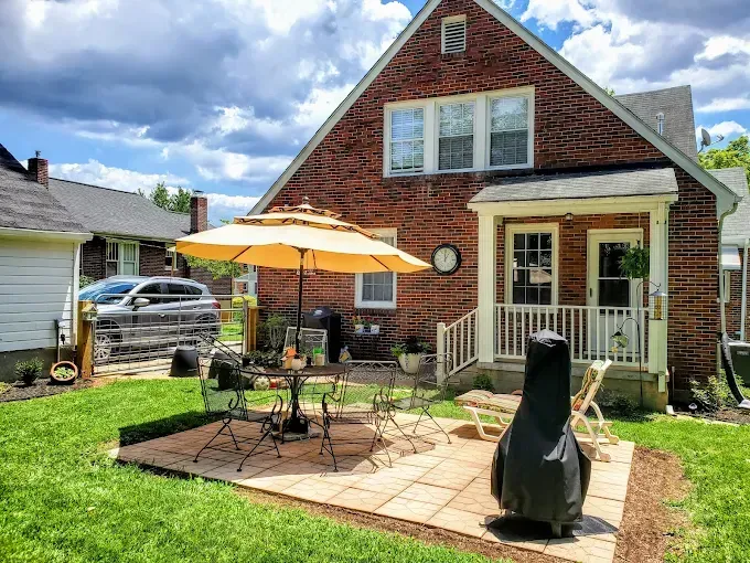 Brick house with patio, umbrella, and outdoor furniture in the backyard on a sunny day.