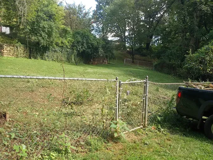 Chain link fence with open gate, grass yard, trees, and black truck.