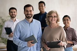Group of diverse professionals smiling, holding notebooks, in an office setting.