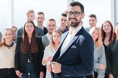 Smiling man in glasses and suit jacket, leading a diverse group of young professionals.