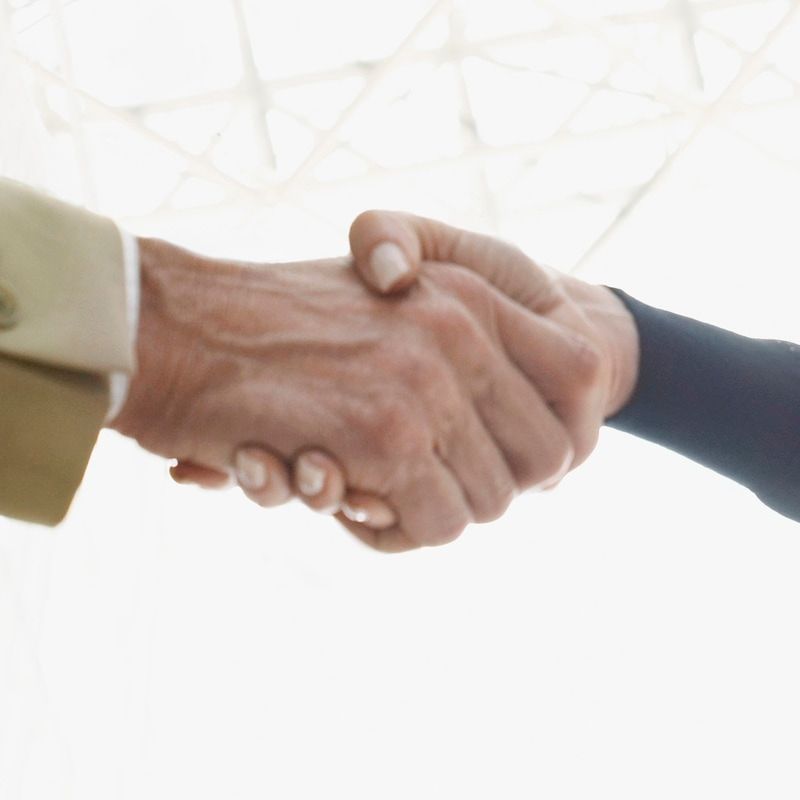 A man in a suit shakes hands with another man in a blue shirt