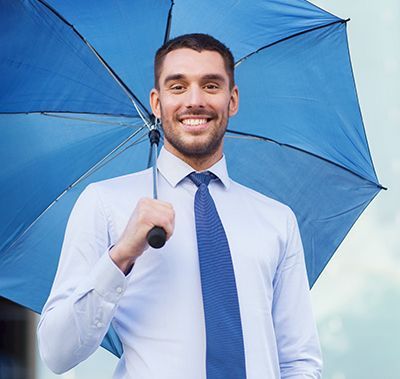 Man in a button-up shirt and tie holding a blue umbrella, smiling outside.