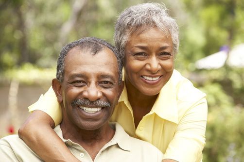 A woman is hugging a man in a park and they are smiling for the camera.