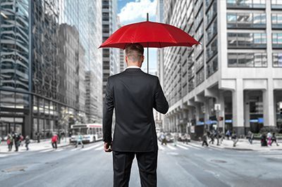 Man in suit holding a red umbrella in a city street, standing with his back to the viewer.