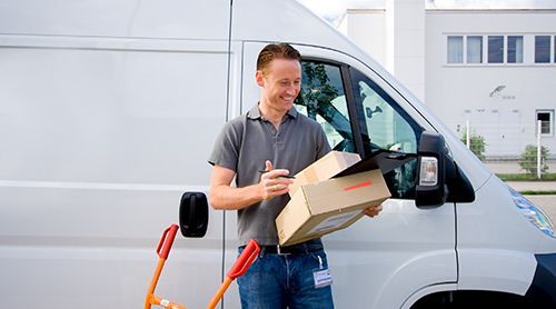 Delivery person, looking at a package next to a white van, outside a building.