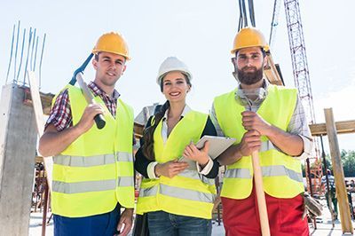 Construction workers in hard hats and vests, smiling at camera on construction site.