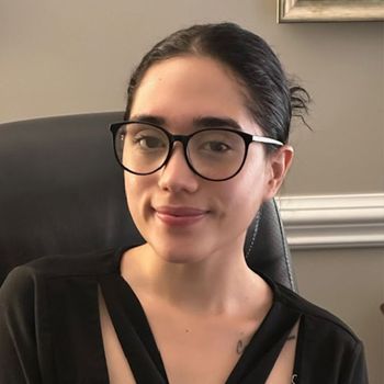 A woman wearing glasses and a black shirt is sitting in a chair.