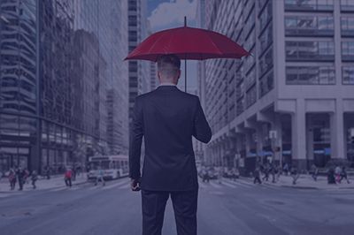 Man in suit holding a red umbrella on a city street, seen from behind.