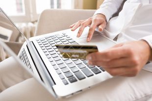 A person is holding a credit card in front of a laptop computer.