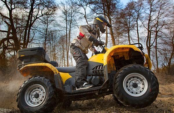 A man is riding a yellow atv in the woods.