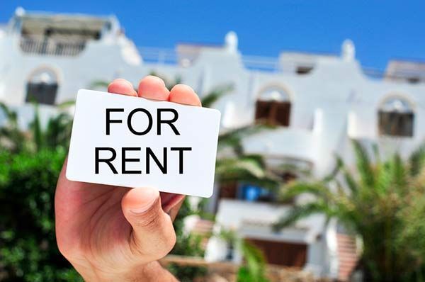 A person is holding a card that says `` for rent '' in front of a house.