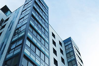 Modern high-rise apartment building with blue tinted windows against a light blue sky.